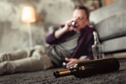adult man lying on carpet in living room with alcohol bottles around